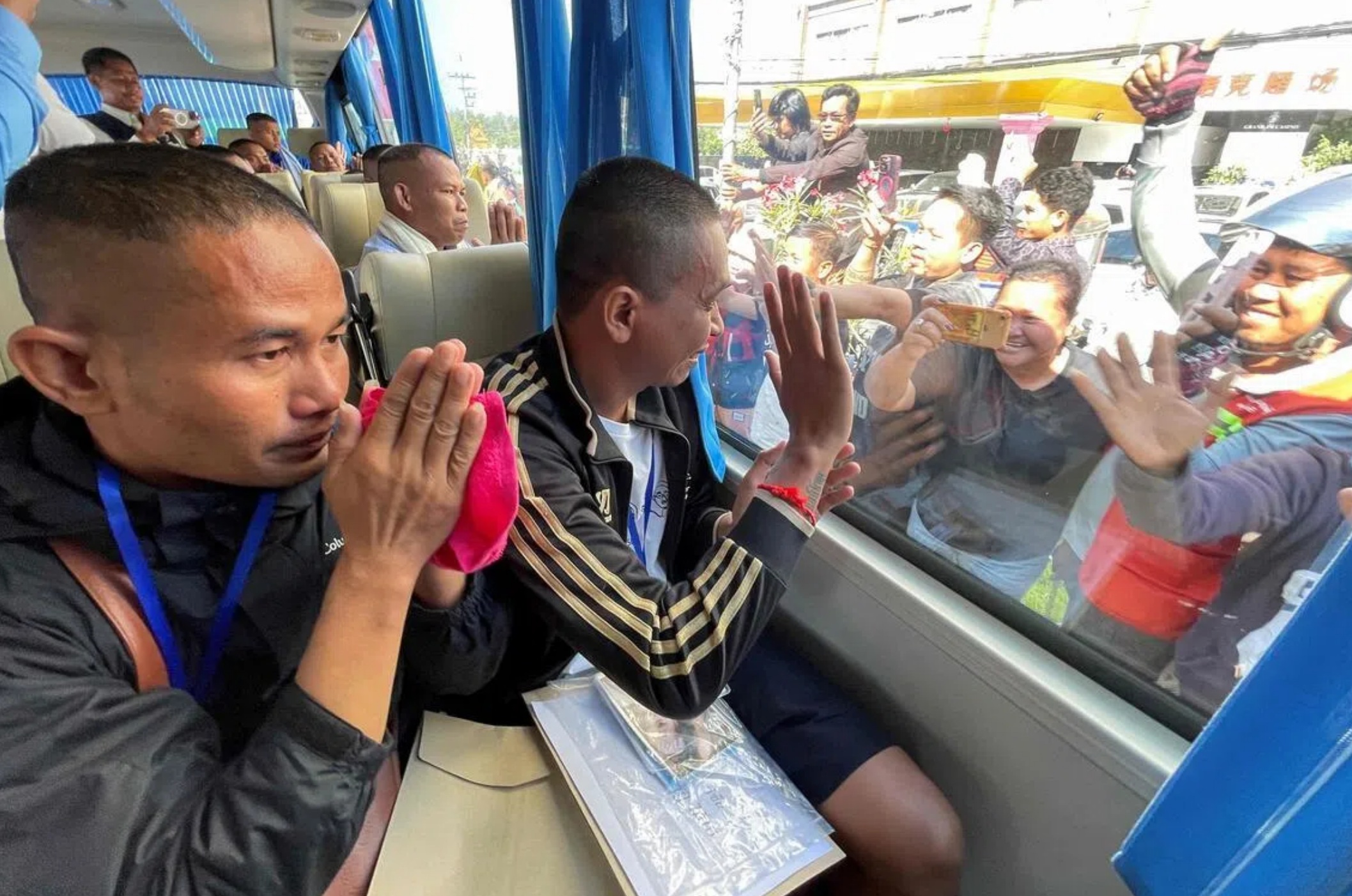 获释的柬埔寨士兵星期三乘坐巴士抵达边境拜林省时微笑着挥手，或双手合十向人群致意 ...